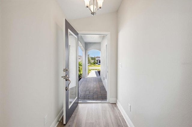 hall featuring a chandelier, lofted ceiling, baseboards, and wood finished floors