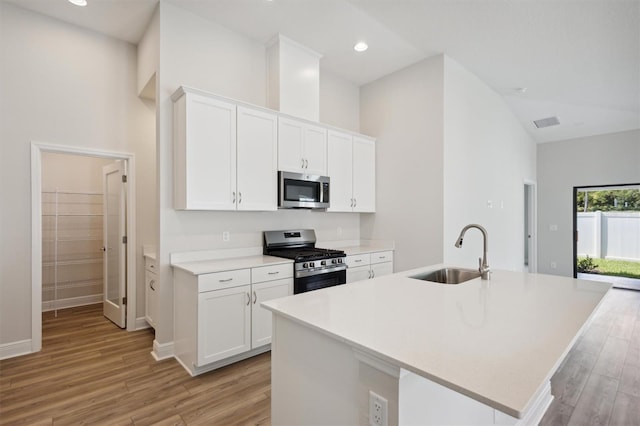 kitchen with high vaulted ceiling, stainless steel appliances, light hardwood / wood-style floors, white cabinetry, and sink