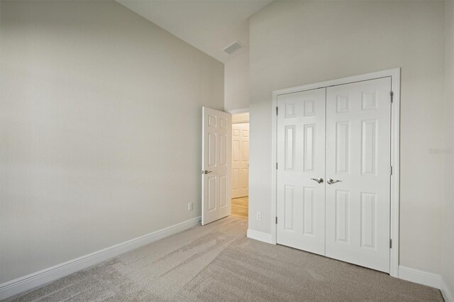 unfurnished bedroom with high vaulted ceiling, a closet, and light colored carpet