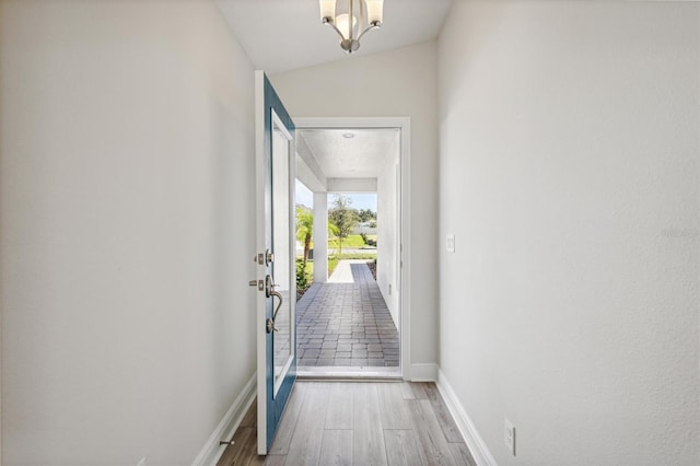 doorway to outside featuring a notable chandelier, vaulted ceiling, and light hardwood / wood-style floors