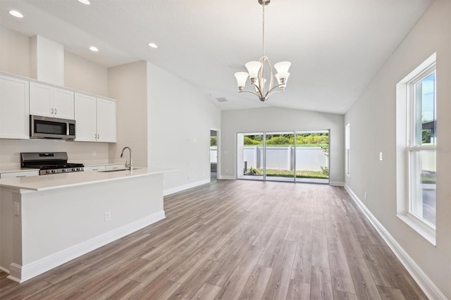 kitchen featuring white cabinets, hanging light fixtures, vaulted ceiling, light hardwood / wood-style floors, and stainless steel appliances