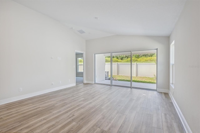 spare room with vaulted ceiling, baseboards, and light wood-style floors