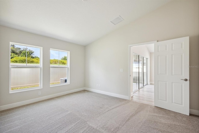 unfurnished room with lofted ceiling, light colored carpet, and a healthy amount of sunlight