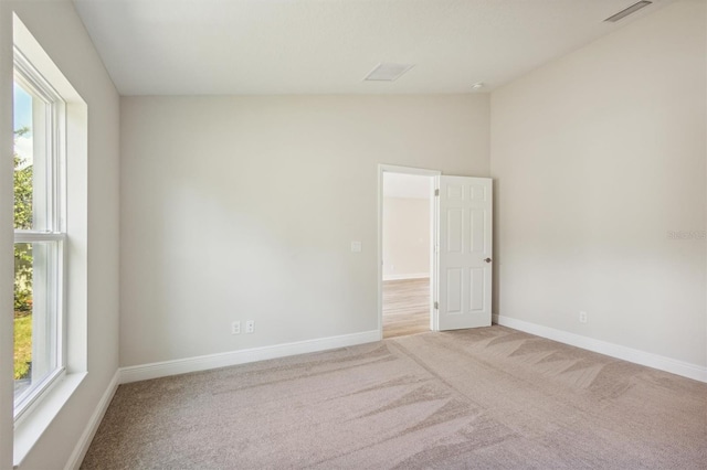 carpeted spare room featuring lofted ceiling, visible vents, plenty of natural light, and baseboards