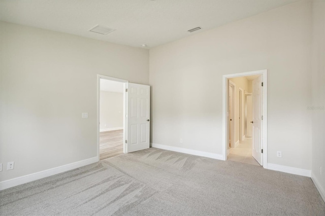 unfurnished room featuring light carpet, baseboards, visible vents, and lofted ceiling