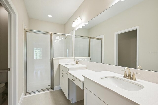 bathroom featuring double vanity, a shower with door, toilet, and tile patterned flooring