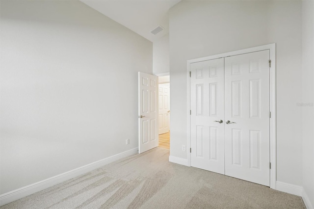 unfurnished bedroom with high vaulted ceiling, a closet, and light colored carpet