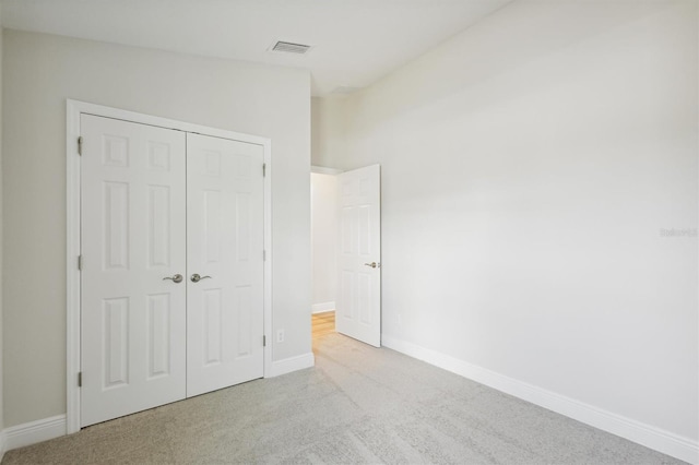 unfurnished bedroom featuring baseboards, a closet, visible vents, and light colored carpet