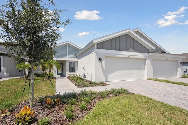 view of front facade featuring decorative driveway, stucco siding, an attached garage, board and batten siding, and a front yard