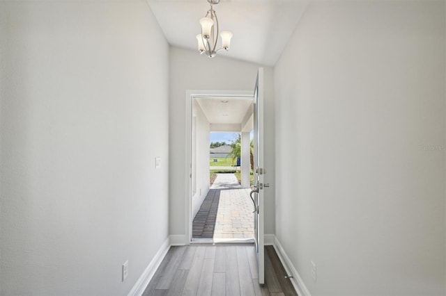 corridor featuring a notable chandelier, vaulted ceiling, and hardwood / wood-style floors