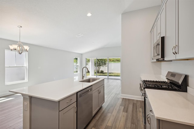 kitchen with appliances with stainless steel finishes, a kitchen island with sink, sink, wood-type flooring, and vaulted ceiling