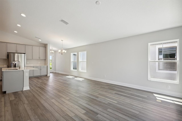 unfurnished living room with lofted ceiling, wood finished floors, visible vents, baseboards, and an inviting chandelier