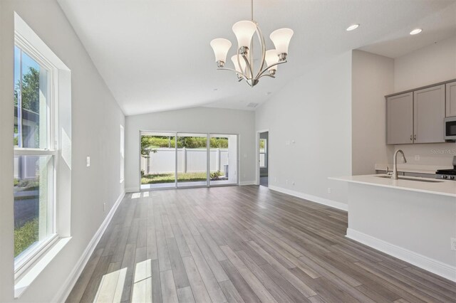 unfurnished living room featuring sink, high vaulted ceiling, hardwood / wood-style floors, and a chandelier