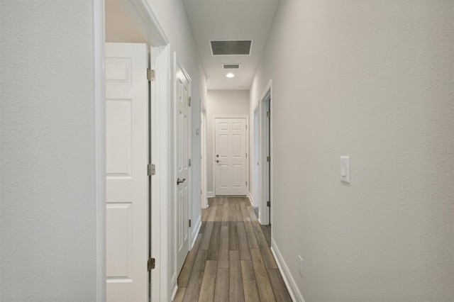 hallway with wood finished floors, visible vents, and baseboards