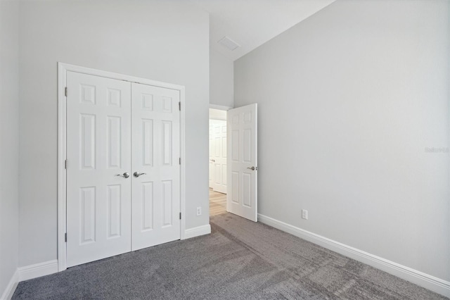 unfurnished bedroom with high vaulted ceiling, a closet, carpet, and baseboards