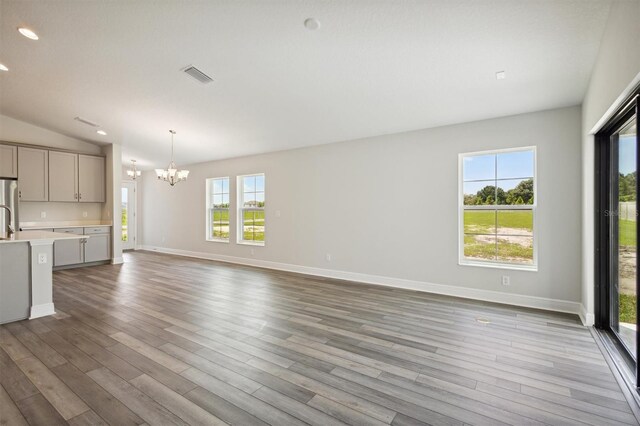 unfurnished living room with vaulted ceiling, light hardwood / wood-style flooring, plenty of natural light, and an inviting chandelier