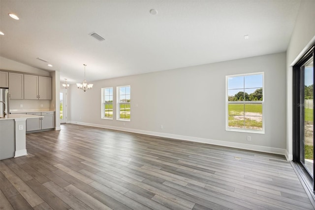 unfurnished living room with light wood-style floors, visible vents, vaulted ceiling, and a notable chandelier