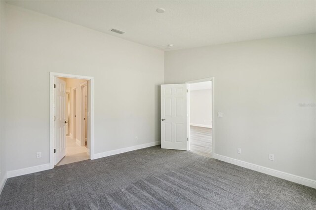 unfurnished bedroom with ensuite bath, light colored carpet, and a high ceiling