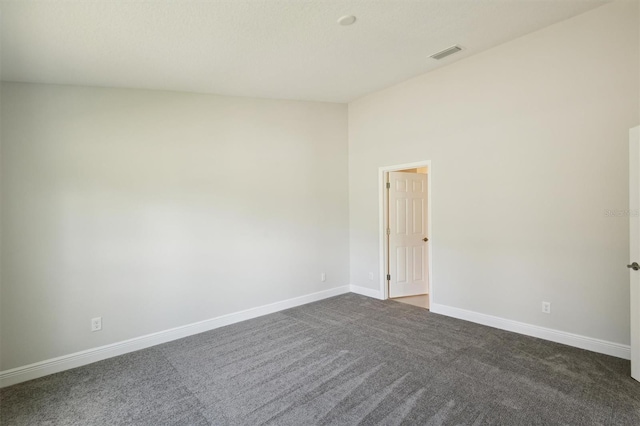 spare room with dark colored carpet, visible vents, and baseboards