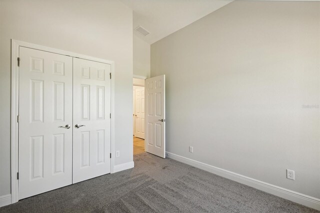 unfurnished bedroom with high vaulted ceiling, carpet flooring, and a closet