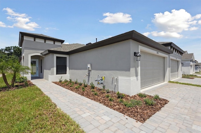 view of front of home with decorative driveway, an attached garage, and stucco siding