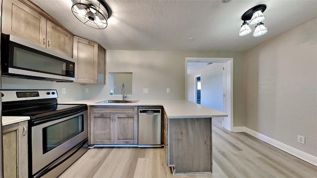 kitchen with appliances with stainless steel finishes, a peninsula, light countertops, light wood-style floors, and a sink