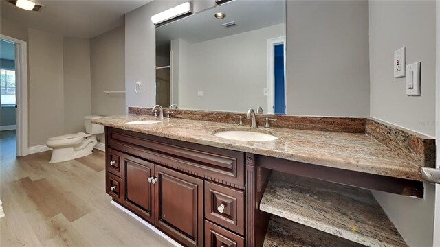 bathroom with toilet, double vanity, a sink, and wood finished floors