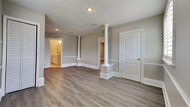 unfurnished bedroom featuring light wood finished floors, decorative columns, baseboards, and ensuite bathroom