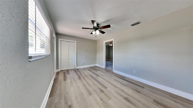 unfurnished bedroom featuring baseboards, visible vents, a ceiling fan, light wood-type flooring, and a closet