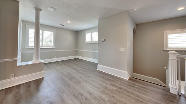 spare room with arched walkways, decorative columns, baseboards, and wood finished floors