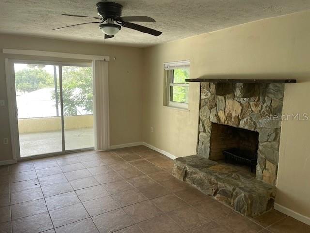 unfurnished living room with tile patterned flooring, ceiling fan, a textured ceiling, and a stone fireplace