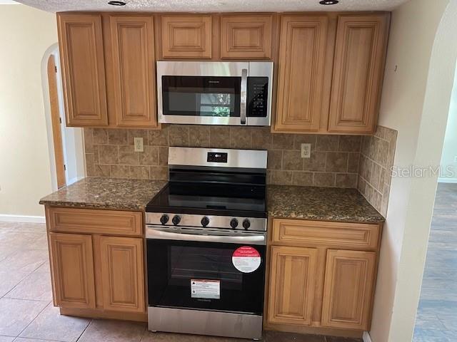 kitchen with dark stone counters, tasteful backsplash, arched walkways, and stainless steel appliances