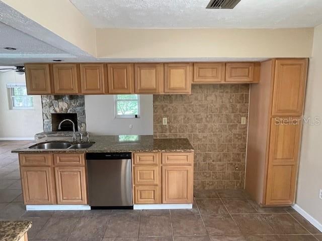 kitchen with stainless steel dishwasher, dark stone countertops, sink, and ceiling fan