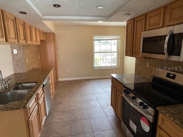 kitchen with a sink, dark stone countertops, appliances with stainless steel finishes, light tile patterned flooring, and baseboards