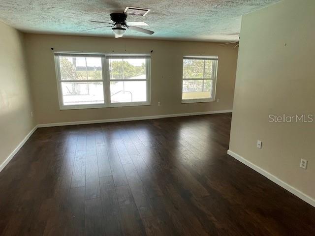 unfurnished room featuring dark wood finished floors, visible vents, a textured ceiling, and ceiling fan