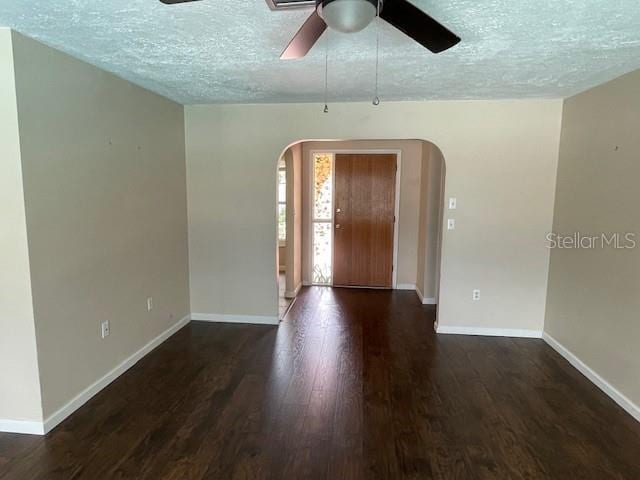 foyer entrance with arched walkways, a textured ceiling, baseboards, and wood finished floors