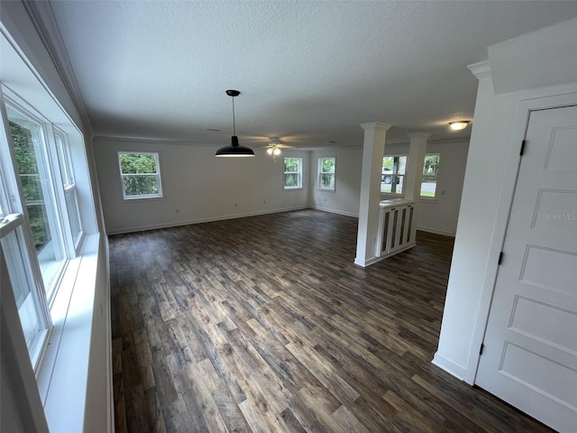 unfurnished living room featuring ornate columns, a healthy amount of sunlight, crown molding, and dark wood-type flooring