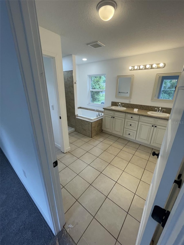 bathroom featuring tile patterned flooring, tiled tub, a textured ceiling, and dual bowl vanity