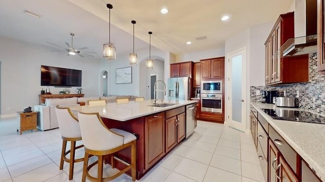 kitchen with ceiling fan, pendant lighting, a center island with sink, appliances with stainless steel finishes, and a breakfast bar area