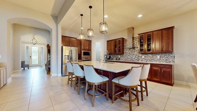 kitchen featuring wall chimney range hood, decorative backsplash, sink, a kitchen island with sink, and stainless steel appliances