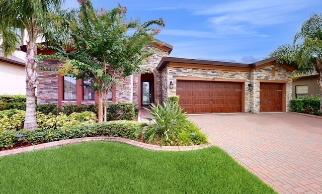 mediterranean / spanish house featuring a front lawn, decorative driveway, stone siding, and a garage