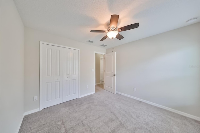 unfurnished bedroom with ceiling fan, light colored carpet, a textured ceiling, and a closet