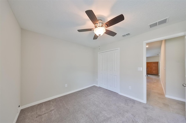 unfurnished bedroom with ceiling fan, light colored carpet, a textured ceiling, and a closet