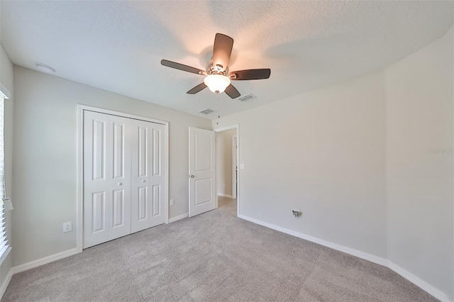 unfurnished bedroom with ceiling fan, light colored carpet, a textured ceiling, and a closet