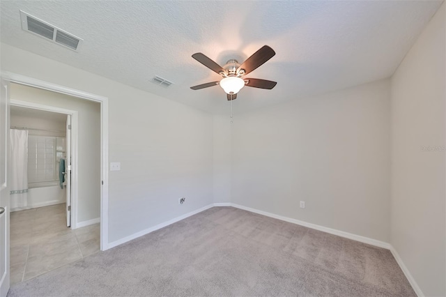 empty room with ceiling fan, light colored carpet, and a textured ceiling