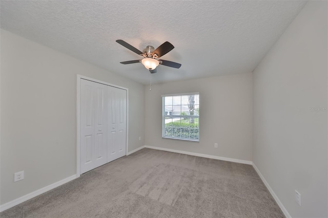 unfurnished bedroom with ceiling fan, light colored carpet, a closet, and a textured ceiling