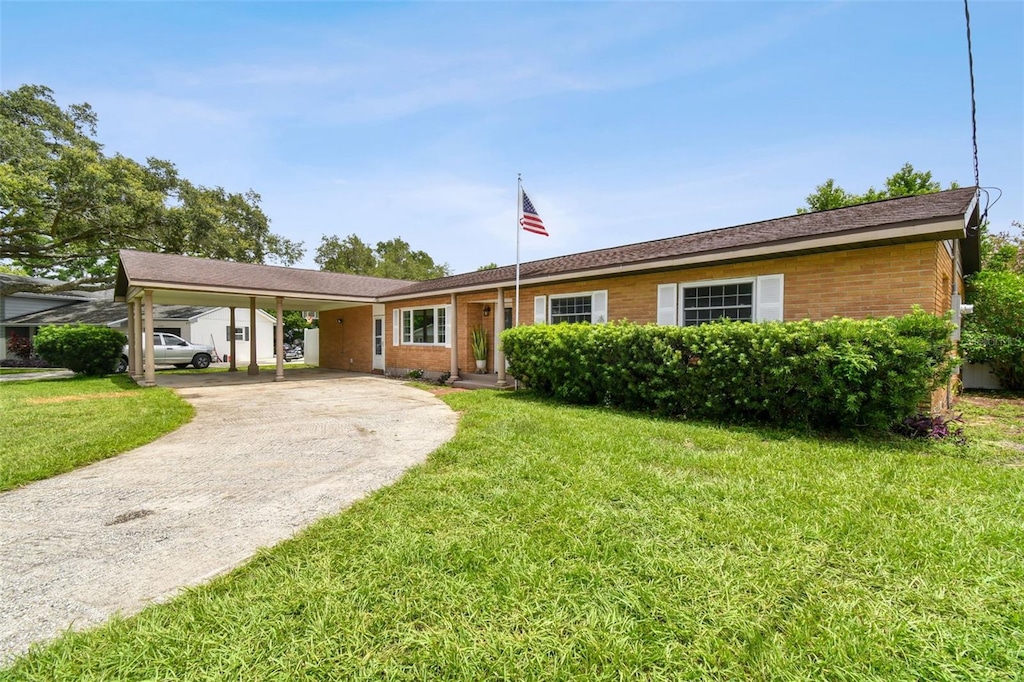 single story home with a carport, concrete driveway, brick siding, and a front lawn