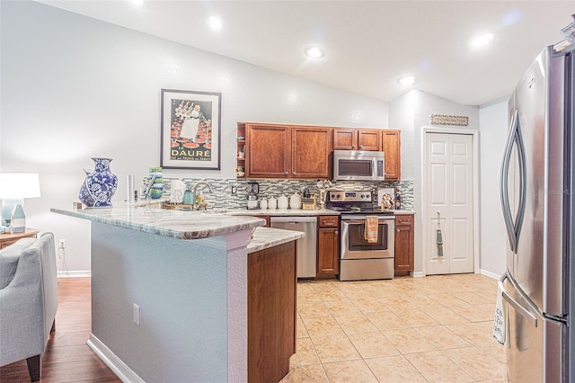 kitchen featuring kitchen peninsula, appliances with stainless steel finishes, backsplash, vaulted ceiling, and light tile patterned floors