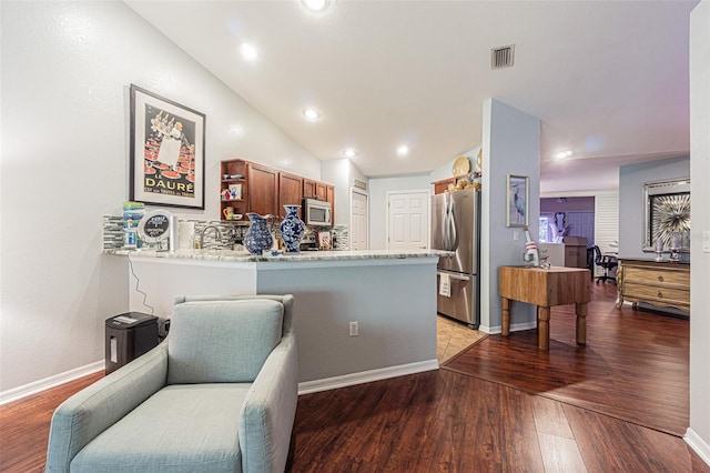 kitchen featuring vaulted ceiling, light wood-type flooring, light stone counters, kitchen peninsula, and stainless steel appliances