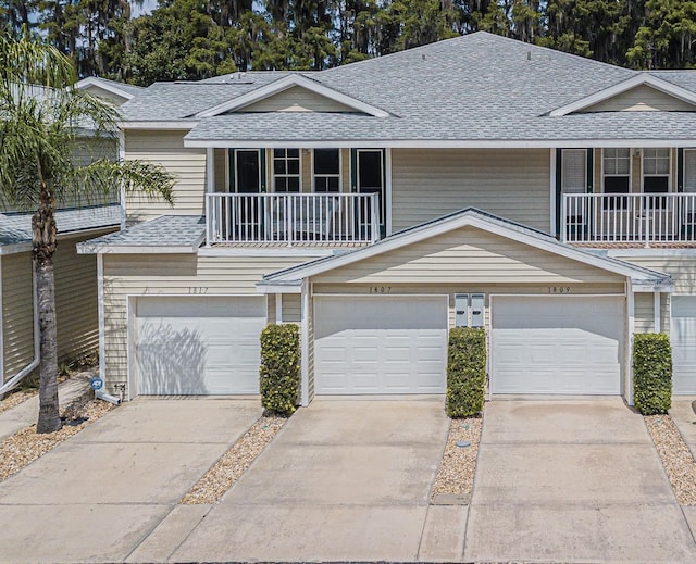 view of property with a garage, concrete driveway, roof with shingles, and a balcony